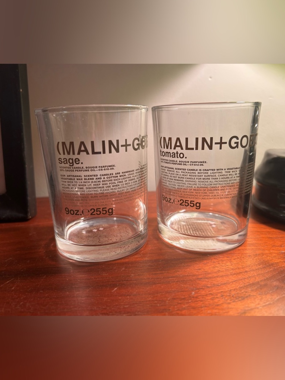 Two empty Malin + Goetz 9 oz. candle jars, Sage and Tomato.